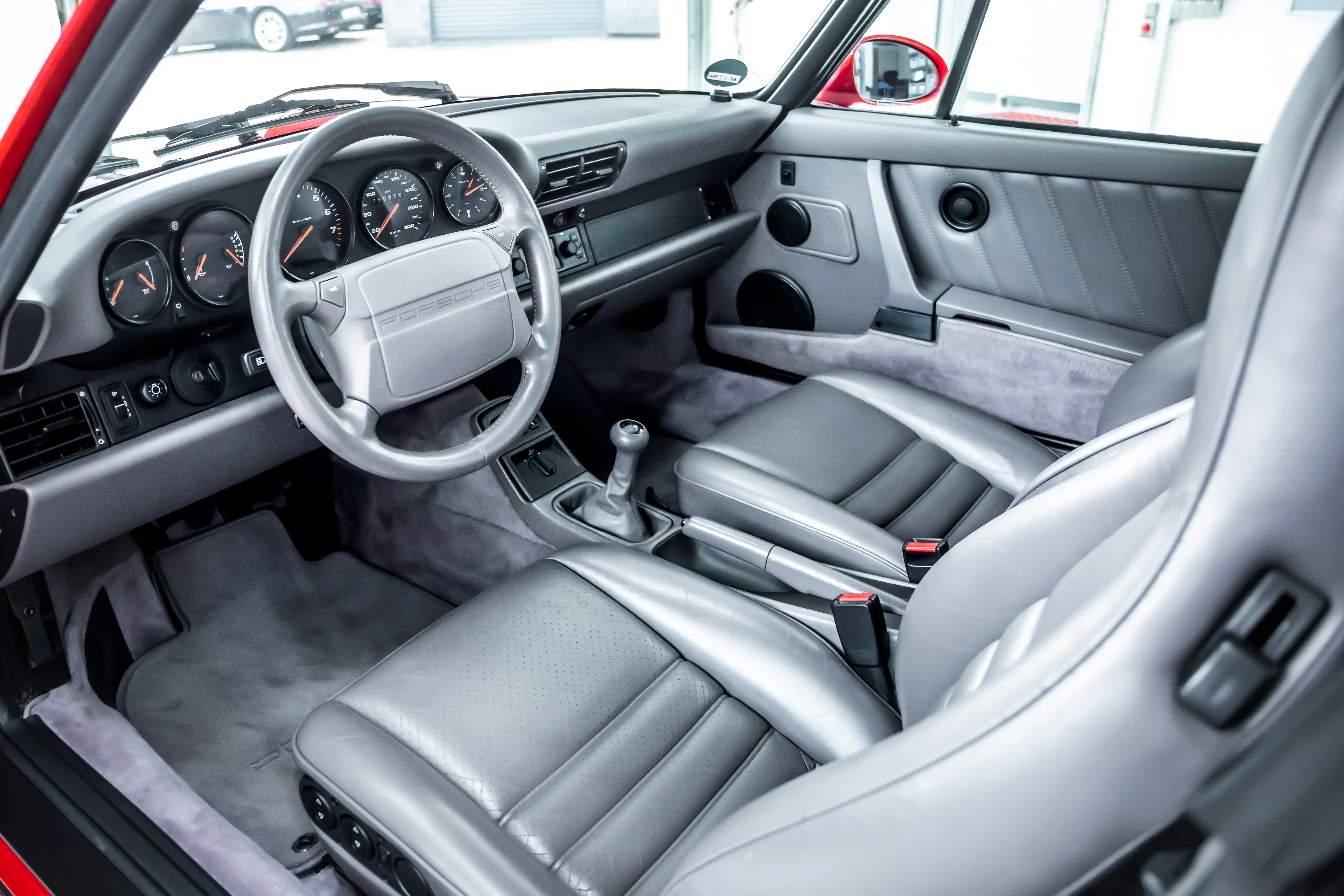 Innenraum des Porsche 964 Carrera 2 mit grauem Ledersitz, Armaturenbrett und Schaltgetriebe