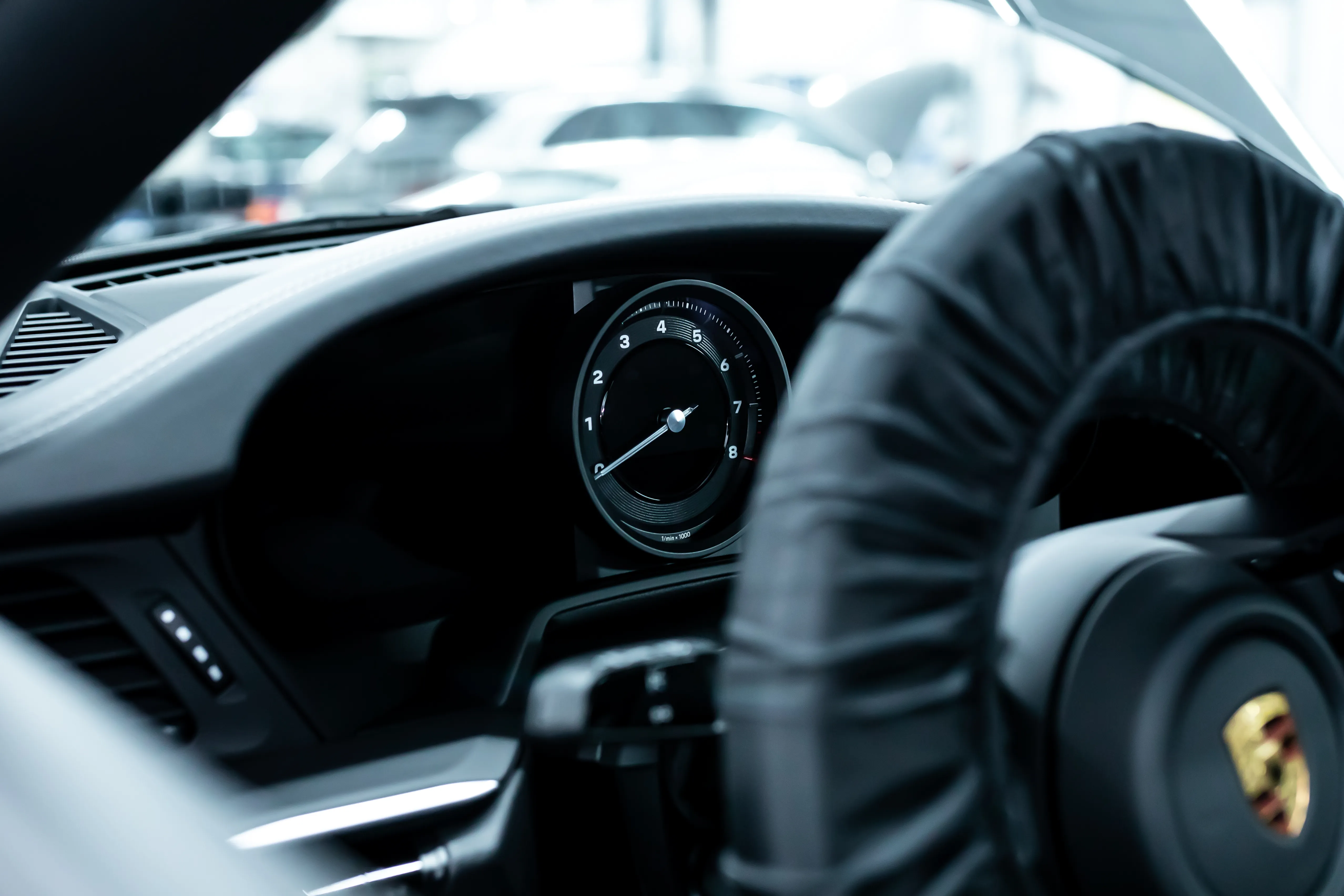 Porsche 911 Turbo Cockpit Detail, analoger Drehzahlmesser und Lenkrad mit Porsche Wappen aus Fahrerperspektive
