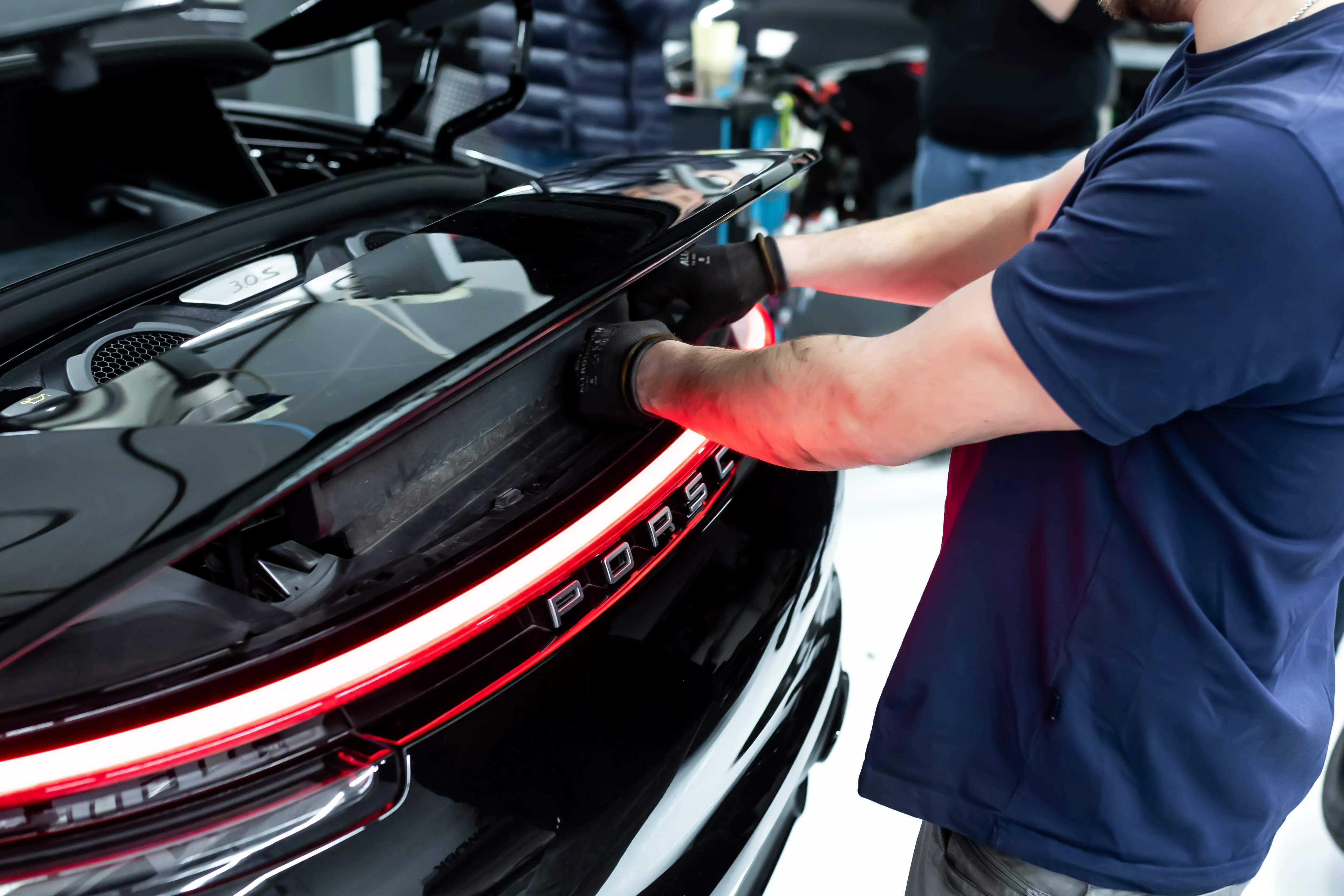 Mechaniker poliert Heckbereich eines schwarzen Porsche 911 Turbo, rote Rückleuchten-Lichtleiste leuchtet